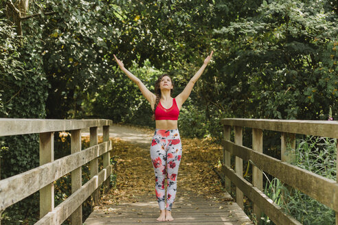 Young woman practicing Pilates in an urban park, raised arms - NMSF00240