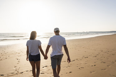 Young couple doing a romantic beach stroll at sunset - UUF15094