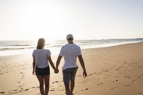 Junges Paar bei einem romantischen Strandspaziergang bei Sonnenuntergang - UUF15094