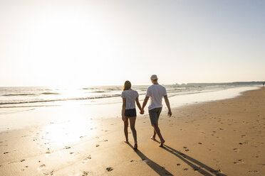 Young couple doing a romantic beach stroll at sunset - UUF15095