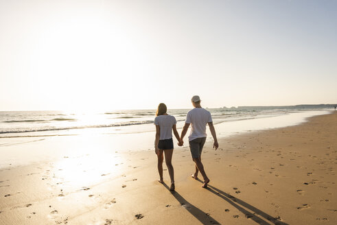 Junges Paar bei einem romantischen Strandspaziergang bei Sonnenuntergang - UUF15095