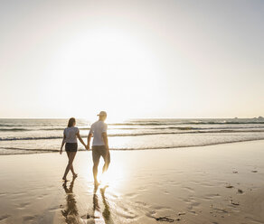 Junges Paar bei einem romantischen Strandspaziergang bei Sonnenuntergang - UUF15096