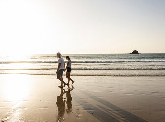 Junges Paar bei einem romantischen Strandspaziergang bei Sonnenuntergang - UUF15097