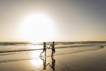 Junges Paar bei einem romantischen Strandspaziergang bei Sonnenuntergang - UUF15098