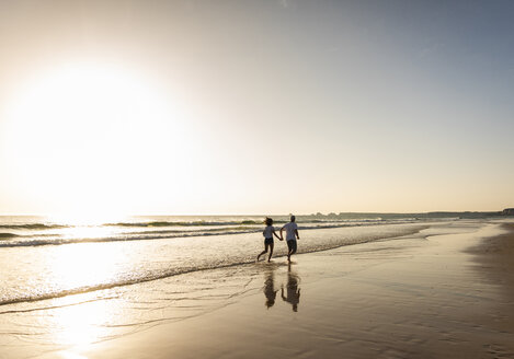 Junges Paar bei einem romantischen Strandspaziergang bei Sonnenuntergang - UUF15099