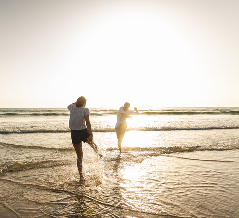 Junges Paar, das sich am Strand vergnügt und im Meer plantscht, lizenzfreies Stockfoto