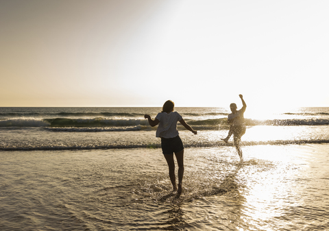 Junges Paar, das sich am Strand vergnügt und im Meer plantscht, lizenzfreies Stockfoto