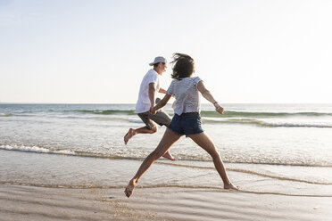 Young couple having fun on the beach, running and jumping at the sea - UUF15106