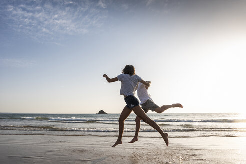 Junges Paar, das sich am Strand vergnügt, rennend und springend am Meer - UUF15107