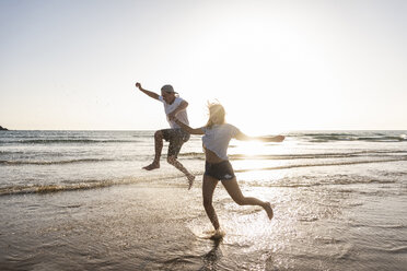 Young couple having fun at the beach, splashing water in the sea - UUF15109