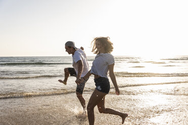 Young couple having fun at the beach, splashing water in the sea - UUF15110