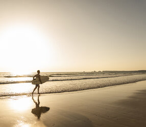 Young man running on beach, carrying surfboard - UUF15113