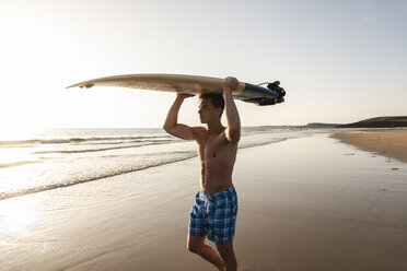 Junger Mann, der am Strand spazieren geht und sein Surfbrett trägt - UUF15117