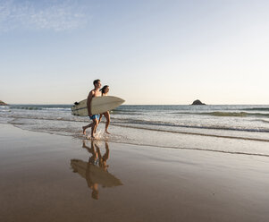 Young couple running on beach, carrying surfboard - UUF15119