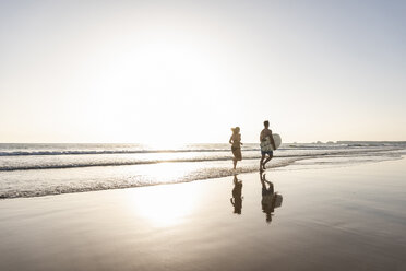 Young couple running on beach, carrying surfboard - UUF15121