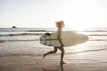 Young woman running on beach, carrying surfboard - UUF15123