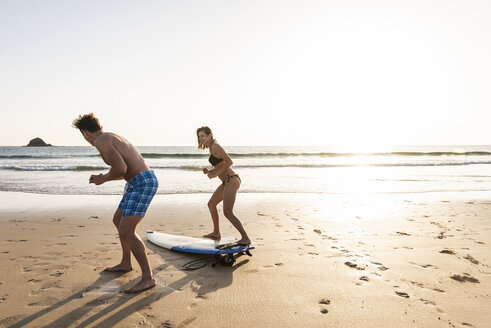 Junger Mann zeigt junger Frau am Strand, wie man surft - UUF15125
