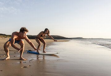 Young man showing young woman how to surf on the beach - UUF15127