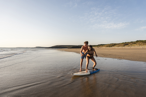 Junger Mann zeigt junger Frau am Strand, wie man surft, lizenzfreies Stockfoto