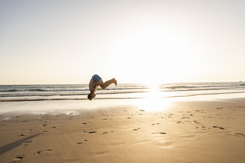 Junger Mann, der am Strand Purzelbäume schlägt, lizenzfreies Stockfoto