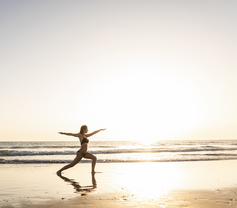 Junge Frau praktiziert Yoga am Strand, sitzt auf einem Surfbrett und meditiert, lizenzfreies Stockfoto