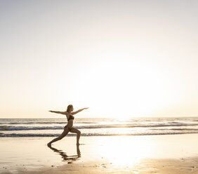 Young woman practicing yoga on the beach, sitting on surfboard, meditating - UUF15142