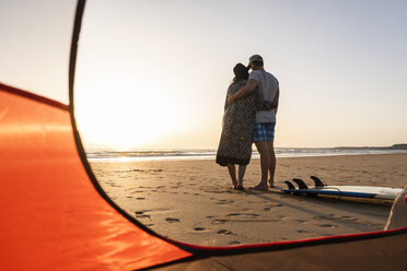 Romantic couple camping on the beach, embracing at sunset - UUF15145