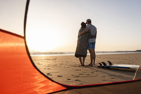 Romantisches Paar, das am Strand zeltet und sich bei Sonnenuntergang umarmt - UUF15145