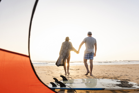 Romantisches Paar, das am Strand zeltet und bei Sonnenuntergang einen Strandspaziergang macht, lizenzfreies Stockfoto