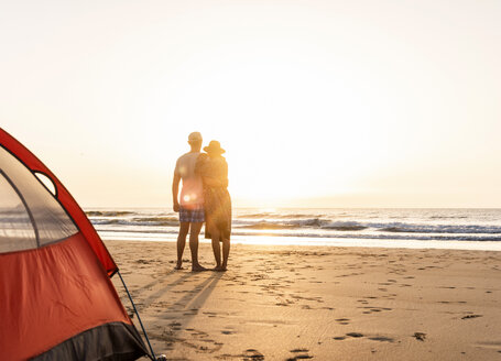 Romantisches Paar, das am Strand zeltet und sich bei Sonnenuntergang umarmt - UUF15153