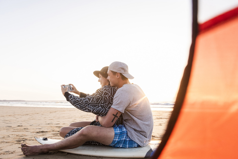 Pärchen zeltet am Strand und macht Smartphone-Selfies, lizenzfreies Stockfoto