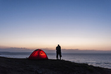 Romantic couple camping on the beach, kissing in twilight - UUF15168