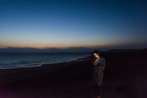 Junge Frau benutzt Smartphone am nächtlichen Strand, lizenzfreies Stockfoto