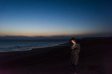 Junge Frau benutzt Smartphone am nächtlichen Strand - UUF15174