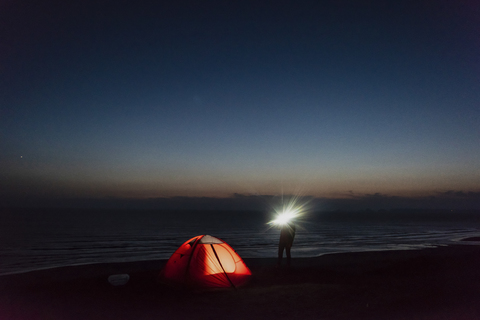 Young man camping on the beach, using flashlight stock photo