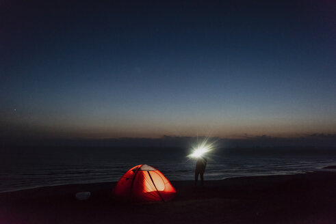 Junger Mann beim Zelten am Strand, mit Taschenlampe - UUF15175