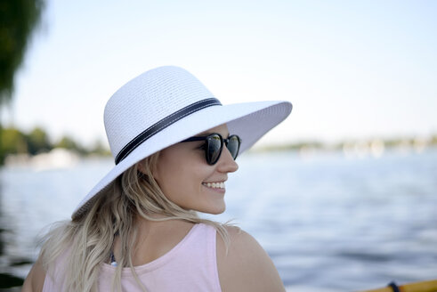 Lächelnde junge Frau mit Sonnenbrille und weißem Sommerhut am See - BFRF01905