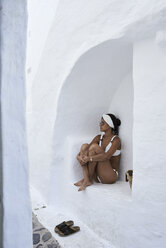 Junge Frau im weißen Bikini sitzt in einer Mauernische - IGGF00595