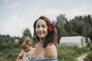 Portrait of mother with flower in her hair with baby in garden - KMKF00548