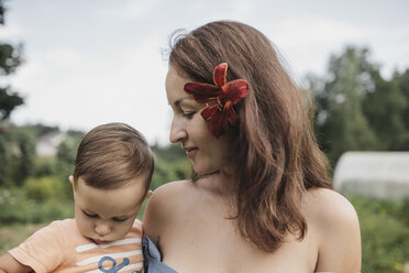 Mother with flower in her hair holding baby in garden - KMKF00549