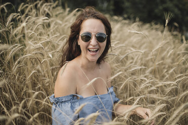 Porträt einer glücklichen Frau mit Sonnenbrille in einem Weizenfeld - KMKF00551