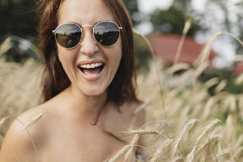 Porträt einer glücklichen Frau mit Sonnenbrille in einem Weizenfeld - KMKF00552