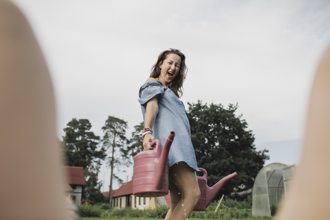 Fröhliche verspielte Frau mit Gießkannen im Garten, lizenzfreies Stockfoto