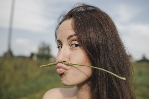 Porträt einer Frau, die einen Pflanzenstängel auf ihrem Mund balanciert - KMKF00560