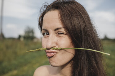 Portrait of woman balancing plant stalk on her mouth twinkling - KMKF00561