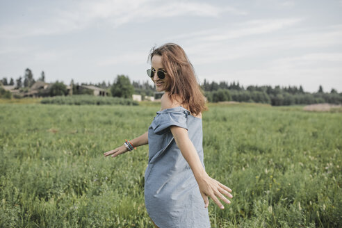 Lächelnde Frau mit Sonnenbrille, die in einem ländlichen Feld spazieren geht - KMKF00562