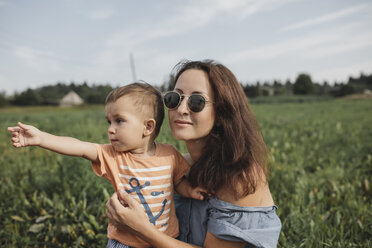 Mutter mit Baby auf einem Feld mit Blick in die Ferne - KMKF00567