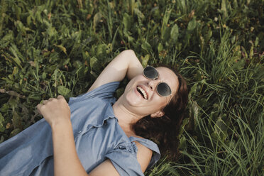 Lachende Frau mit Sonnenbrille im Gras liegend - KMKF00569