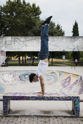 Junger Mann macht einen Handstand auf einer Bank im Skatepark - MAUF01709