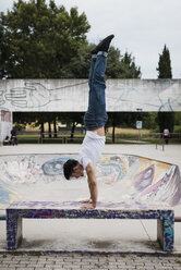 Young man doing a handstand on bench in skatepark - MAUF01709